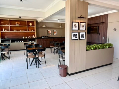 Salão do café da manhã, com mesas, estante de madeira e coluna de quadros