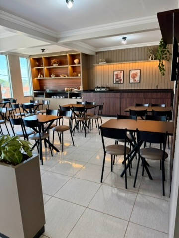 Salão do café da manhã visto do corredor, com mesas e jardineira